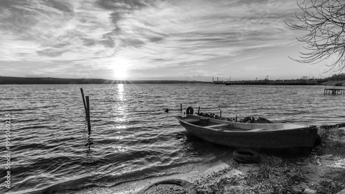 Serene Black and White Sunset Over a Calm Lake with a Rowboat on the Shore
