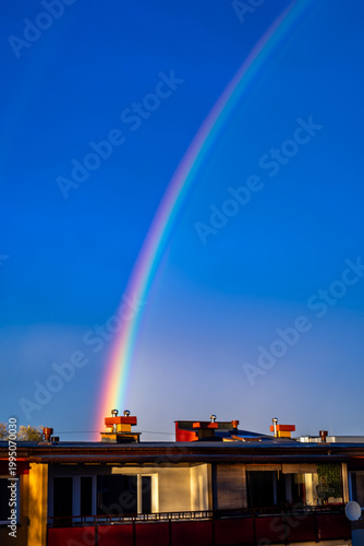 A colorful rainbow over apartment buildings against a dark blue sky. Dark skies after a storm.