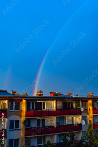 A colorful rainbow over apartment buildings against a dark blue sky. Dark skies after a storm.