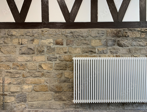 Heating radiator mounted on a rustic stone wall. Home interior and temperature control concept