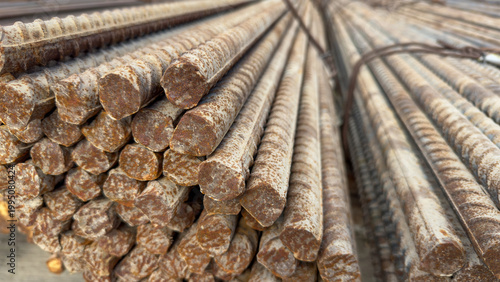 A large stack of ribbed steel reinforcement bars shows signs of rust and weathering. Heavy construction materials, industrial engineering, building foundation.