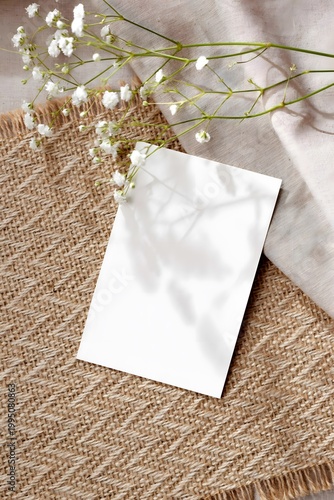 Minimal rustic mockup with blank card and delicate white flowers on natural fabric
