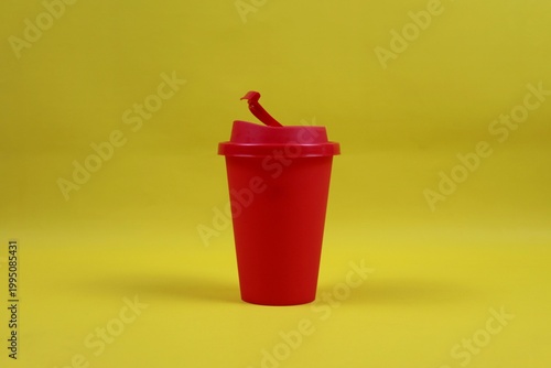 Red plastic coffee cup with lid on a yellow background, minimal studio composition representing takeaway coffee concept.