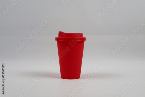 Red plastic coffee cup with lid on a white background, minimal studio composition representing takeaway coffee concept.