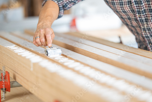 Carpenter applying wood glue with roller on planks