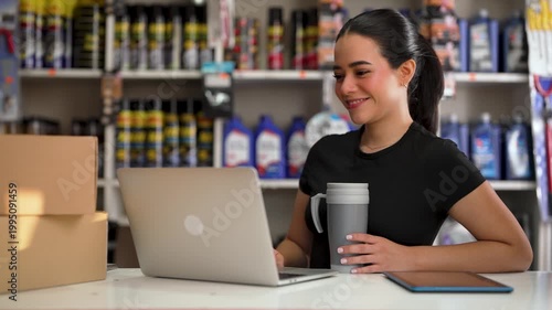 Happy young woman working at her small business, smiling while using her computer in a store