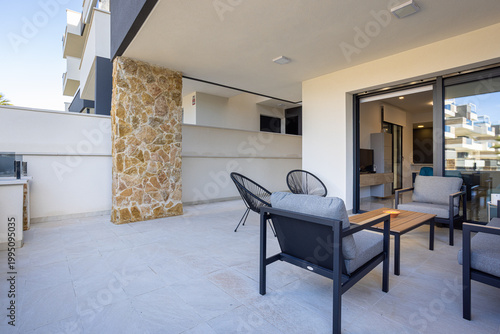 Modern outdoor terrace with lounge furniture, stone column and spacious covered patio in contemporary apartment