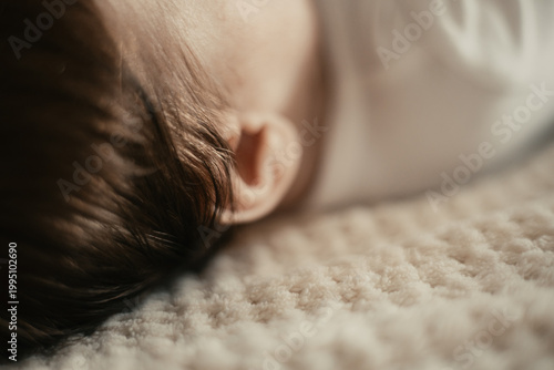 Close-up of the back of the head of an infant with dark hair, lying on a bright, textured blanket in the home interior