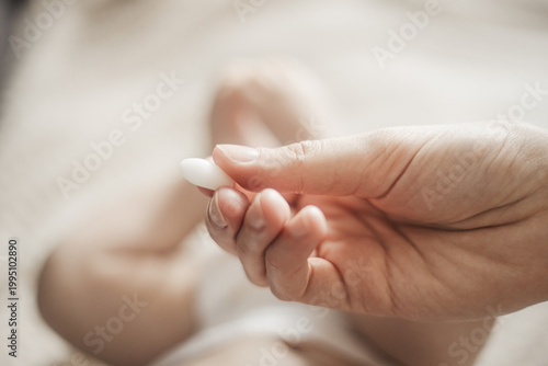 Close-up of a hand holding a white suppository against the background of an infant lying at home