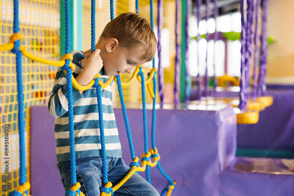 Fototapeta premium Young boy climbing rope structure at indoor playground
