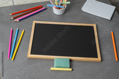 Blank blackboard and writing tools on a gray table in an indoor workspace setting during daytime hours
