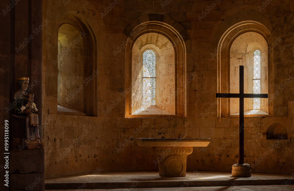 Obraz premium Le Thoronet, Var, France : Romanesque chapel interior with stone altar, cross silhouette and stained glass windows in warm spiritual light