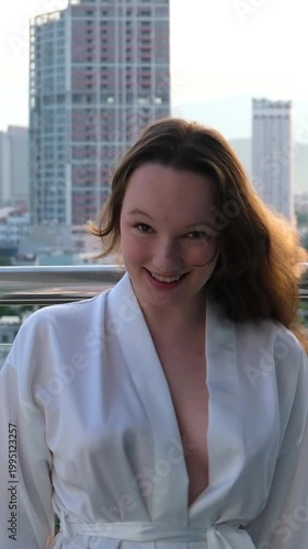 A beautiful luxury woman in a white dress enjoys the sunset view behind the modern skyline of Downtown Vietnam Danang with a drink