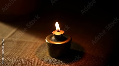 Flickering candle in a brass holder casting warm light on a textured surface. Ideal for creating a cozy and intimate atmosphere in home decor or events