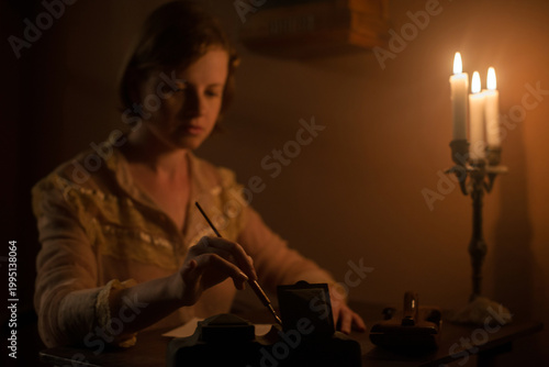 Young woman holding a dip pen writing a letter under candle light