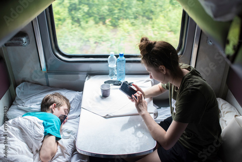 Tableau sur toile Teenager siblings traveling by long distance train using smartphones in compartm