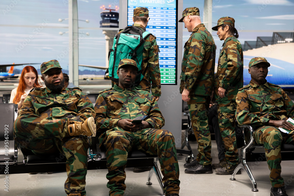 Fototapeta premium Military troops team in airport terminal sitting on bench, waiting for plane arrival. Multiracial army squad wearing camouflage uniforms bored in airport hub after flight got delayed