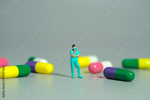 Miniature people toy figure photography. A men doctor or nurse thinking in the middle of medicine pills. Isolated grey background
