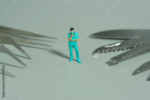 Miniature people toy figure photography. A men doctor or nurse thinking about medical surgery tools. Isolated grey background