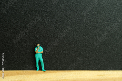 Miniature people toy figure photography. A men doctor or nurse thinking, standing on wooden blackboard