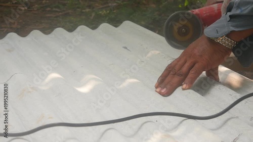A construction worker uses a hand grinder to cut asbestos or fiber cement roofing sheets.