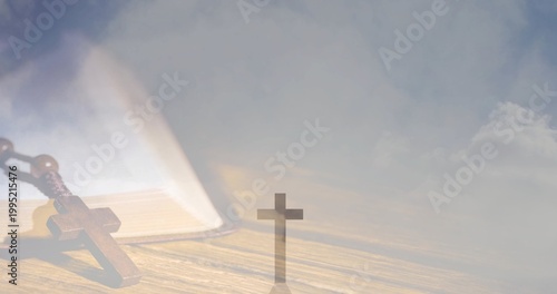 Resting wooden rosary and open book lying on wooden tabletop, with small upright cross silhouette