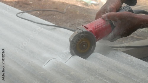 A construction worker uses a hand grinder to cut asbestos or fiber cement roofing sheets.