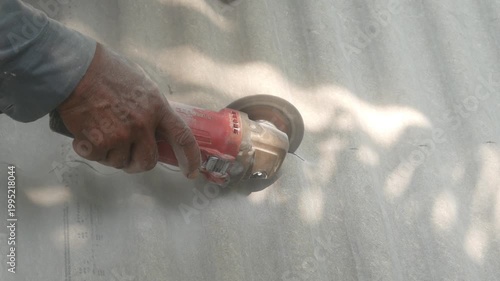 A construction worker uses a hand grinder to cut asbestos or fiber cement roofing sheets.