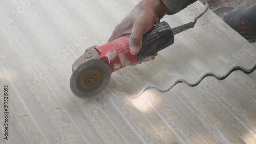 A construction worker uses a hand grinder to cut asbestos or fiber cement roofing sheets.