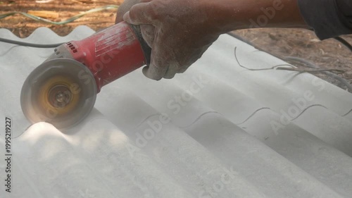 A construction worker uses a hand grinder to cut asbestos or fiber cement roofing sheets.