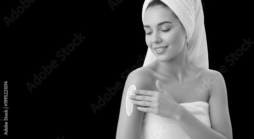 Beautiful young woman applying body lotion on her shoulder, isolated on black background