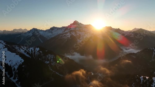 Aerial view captures a majestic mountain range at sunrise, with snow-capped peaks and vibrant sky