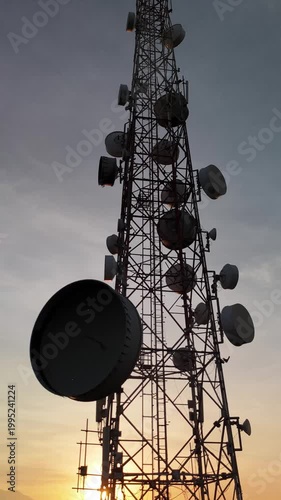 Low angle view of telecommunication tower silhouette with microwave dishes during golden sunrise - Vertical Video
