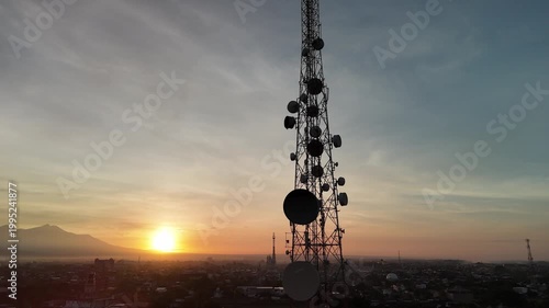 Telecommunication tower silhouette with microwave dish antennas against a golden sunrise city skyline