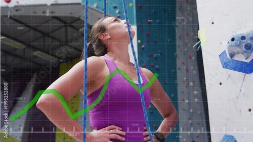 Woman eyeing wall gripping blue rope testing tension readying climb as green sport graph overlaying