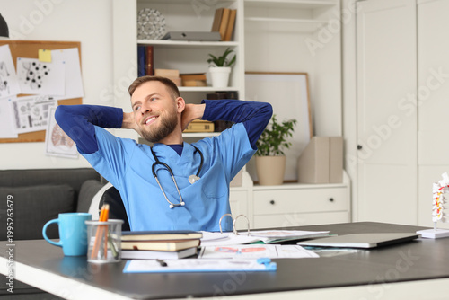 Handsome medical intern sitting at table in clinic