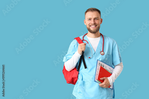 Handsome medical intern with backpack and notebooks on blue background