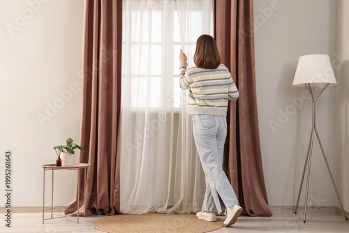Young woman opening curtain...