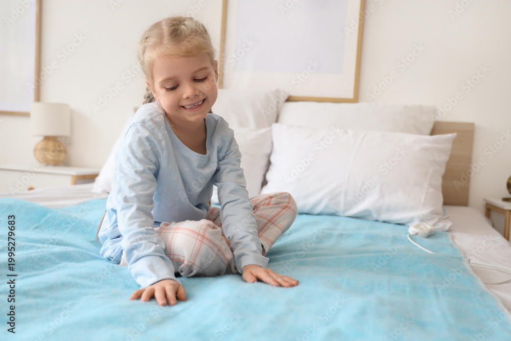 Fototapeta premium Cute little girl sitting on electric heating pad in bedroom