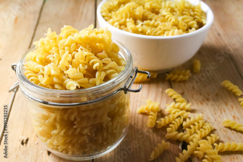 fusilli pasta in a jar and bowl on a wooden table
