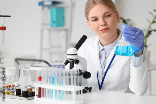 Female scientist with chemical flask and microscope working in laboratory