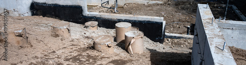 Construction site on new home build, housing development, foundation work in progress with concrete walls poured, round forms, piping and underground water works in place
