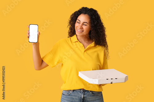 Female African-American courier holding cardboard box with tasty pizza and mo...