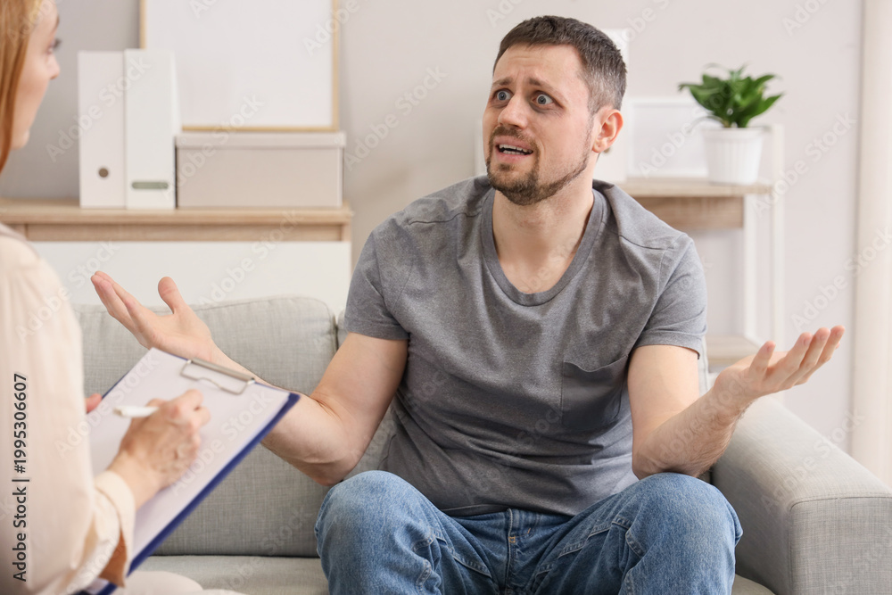 Fototapeta premium Male drug addict talking to psychologist on sofa in office