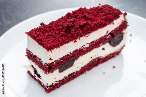 A decadent slice of red velvet cake, artfully layered with fluffy white cream cheese frosting and generous cherry inclusions in Tirana, Albania.