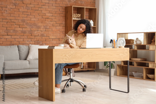 Beautiful young happy African-American woman working with laptop and her cute...
