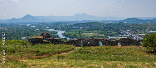 A broad panoramic vista from Rozafa Castle ruins, revealing the winding Buna River, expansive green valley, and distant mountain ranges in Shkoder, Albania.