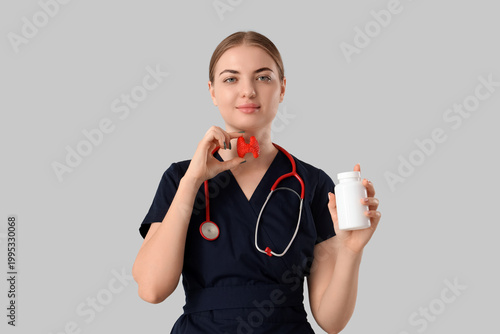 Female endocrinologist with thyroid gland model and pill bottle on grey backg...