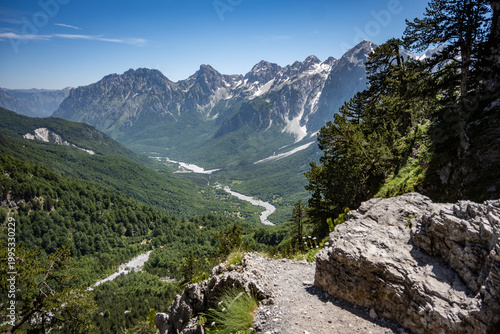 Schilderij op canvas A high-angle view captures the sweeping Valbona Valley, where a river meanders through vast green forests, culminating in sharp, snow-dusted mountain peaks in Albania
