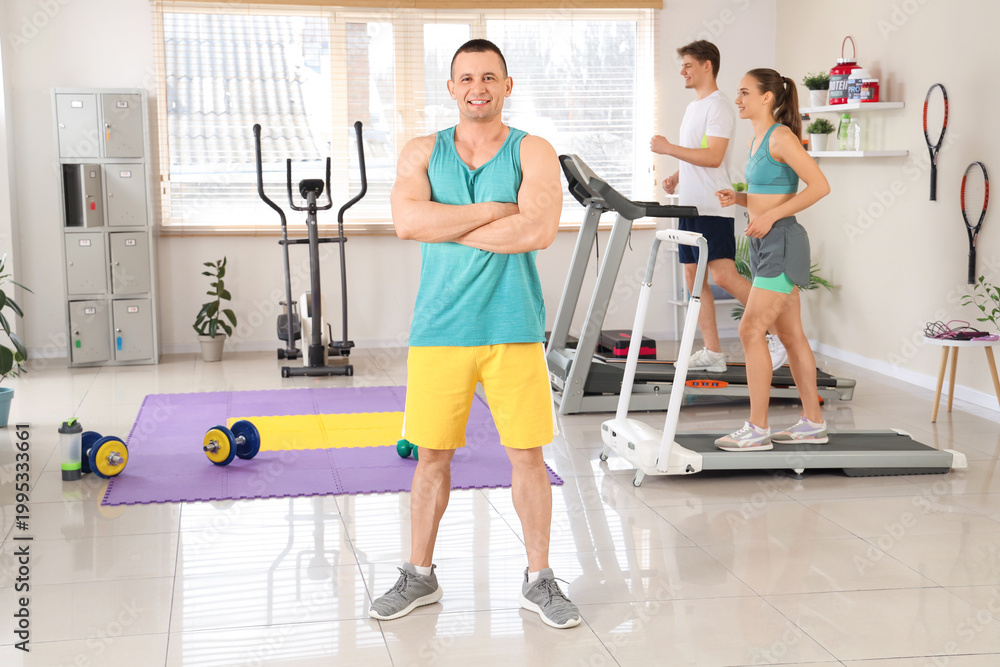 Fototapeta premium Male coach with young people running on treadmills in gym